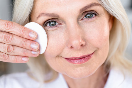 Closeup of middle aged woman with radiant healthy skin cleansing face with delicate tonic. Female remove makeup with cotton pad. Daily skincare proceduresの写真素材