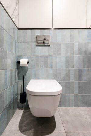 Modern wall hung toilet with seat and closed lid in stylish bathroom. Ceramic wc bowl with concealed cistern and water flush button at domestic restroom with tiled floor.の写真素材