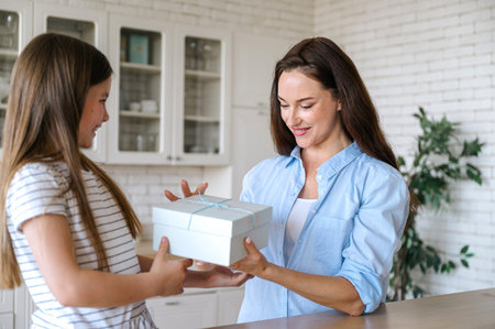 Smiling kid holding present box and congratulating mother with birthday, mothers day or special event. Standing in modern kitchen. Happy family momentsの写真素材