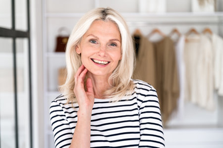 Portrait of smiling mature woman in stylish clothes standing over open wardrobe background. Female stylist glad to present new collection of apparel at fashionable boutiqueの写真素材