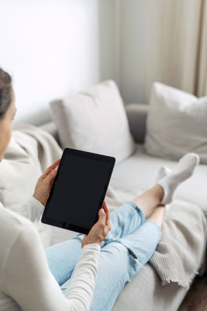 Over shoulder view of woman holding digital tablet computer with empty display. Vertical shot of female using portable device, surfing online, look at copy space on web pageの写真素材