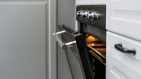 Selective focus on black opened door with metal handle of modern electric oven. Cooking food at home. Kitchen with built in household appliance, baking equipment conceptsの写真素材