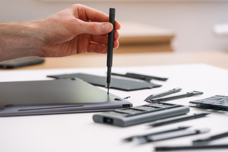 Engineer inspecting disassembled broken laptop, remove cover to checking motherboard, replace battery or keyboard. Man holding screwdriver, open case on computer to diagnostic componentsの写真素材