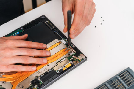 Man repairing an electronic device with screwdriver tool. Repairman working in laptop service. Worker remove broken components from pc, upgrade motherboard on netbook, change battery in digital tabletの写真素材