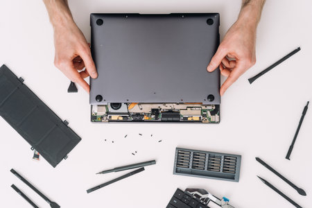 Flat lay view of man open laptop cover in service center. Repair broken elements on pc. Repairman change battery on digital tablet, top view. Man holding a notebook device with both handsの写真素材