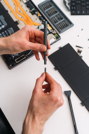 Man puts a small replacement bit on a screwdriver. Man holding hand tool over laptop with a cracked screen and broken battery. Warranty service for broken computerの写真素材