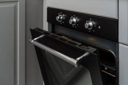 Closeup on electric oven with open door and control panel with knob for adjusting temperature to cooking at kitchen. Modern household appliances. Bake concept. Domestic contemporary cookerの写真素材