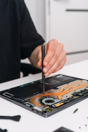 Service of digital devices. Professional technician use screwdriver to replace damaged components inside of pc. Man unscrewing screw on laptop computer to remove and recycle old batteryの写真素材