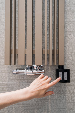 Vertical shot of woman hand adjusting temperature on heated towel rail. Metal heating warmer hanging on bathroom wall. Concept of minimizing energy consumption at homeの写真素材