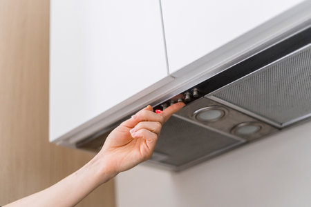 Woman hand push button and select speed of ventilation on control panel at modern extractor hood while she cook food at home. Low angle view of household appliance, metal filter in kitchen extractorの写真素材