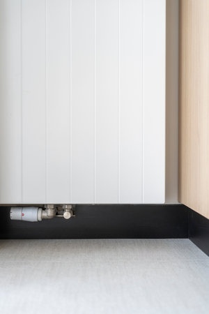 Vertical shot of white metal radiator for central heating with adjustment regulator in modern living room at home.Concepts of controlling temperature in houseの写真素材