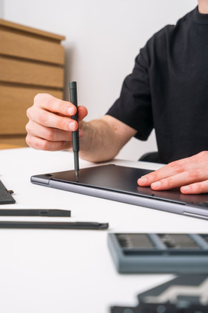Engineer holds a screwdriver in his hands, removes laptop cover to change keyboard or battery. Repairman unscrewing digital tablet case for maintenance. Warranty service conceptsの写真素材
