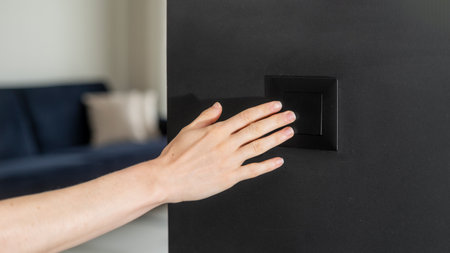 Cropped shot of woman hand turning on or off on plastic light switch with black background of interior wall at home, house or hotel. Copy space.の写真素材