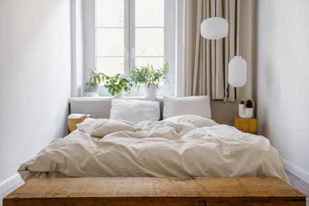 Selective focus on empty wooden bench next to comfortable double bed with duvet and pillows in cozy bedroom. Bohemian style room interior at cozy home. Copy space.の写真素材
