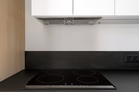 Modern household appliances. Closeup of glass ceramic electrical stove on black countertop and extractor hood at stylish kitchen with contemporary interior. Empty induction hob with control panelの写真素材
