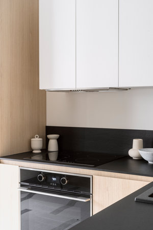Detail in kitchen with luxury interior, electric oven, glass ceramic induction hob, extractor hood integrated in cupboard and ceramic vase with kitchenware on countertop. Modern household appliancesの写真素材
