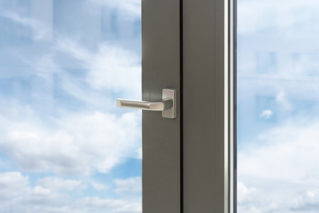 Closeup on closed pvc window with silver handle and view on blue sky through transparent glass. Detail in interior. Advertising concept.の写真素材