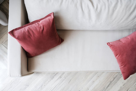 Flat lay view on white soft couch in classic style on wooden floor. Couch with red cushions. Stylish modern furniture and decor in living room at home. Comfortable place to sit and restの写真素材