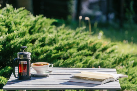 Cup of coffee, french press and an open book on a wooden table in a garden. Cozy picnic on backyard. Concepts of recreation area in public park or summer terrace in cafe, copy space backgroundsの写真素材