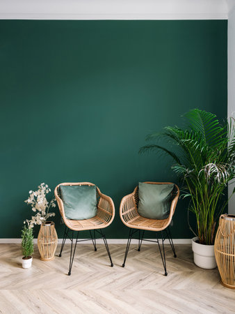 Vertical shot of living room with bohemian style interior design. Rattan armchairs with cushions against green wall. Potted houseplants on laminate. Cozy place for sit and rest at home. Copy space.の写真素材