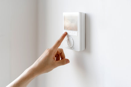 Cropped view on woman hand press button and adjusting temperature at home on room thermostat wich hanging on white wall. Modern device with automatic heat regulation at house.の写真素材