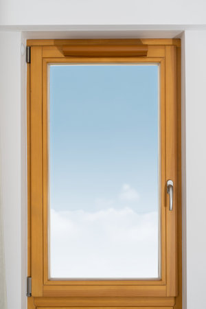 A window with a wooden or plastic frame and a view of a clear blue sky with clouds in living roomの写真素材