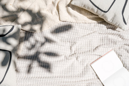 An open book with blank pages lies on a picnic blanket in the shade of trees. Top view at textile decor, plaid and cushion with copy spaceの写真素材