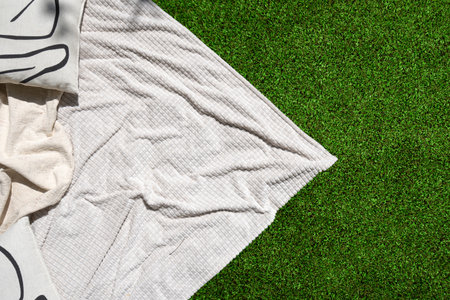 Flat lay shot of white blanket lies on green grass, creating a simple and elegant scene. Garden with plaid and decorative cushion on lawn. Recreation area on backyard. Summer vacation conceptsの写真素材
