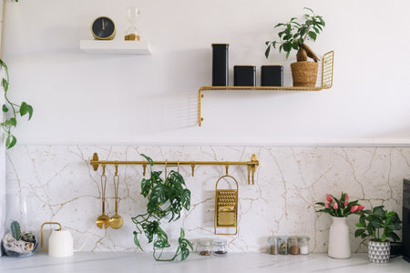 A bright kitchen showcases a marble countertop, golden shelves, potted plants, home decor and stylish storage, creating a serene and modern ambiance in roomの写真素材