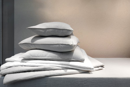 Housekeeping, laundry day concept. Clean bedding, memory foam pillows in french pillowcases and down blanket on mattress in bedroom. Textile on bed, blanket and cushions against copy space backgroundの写真素材