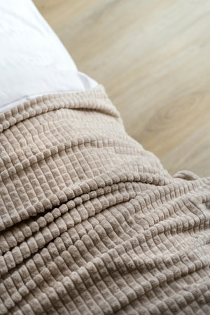 Close up of a beige waffle plaid folded on bed. Light bedroom textile for comfort living at home. Soft blanket on couch against wooden copy space floor in room, vertical viewの写真素材