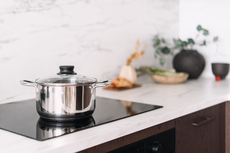 Glass ceramic stove with metal pot. Close up view of electric cooker with stainless steel pan on...