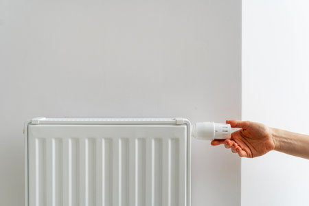 Person adjusting thermostat on radiator making comfortable temperature in room. Central heating system in modern buildings. Concept of consumption of natural resources, energy saving and heat deficitの写真素材