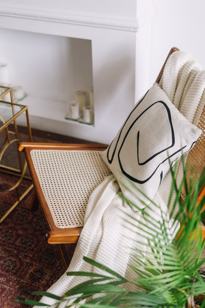 Soft plaid and decorative cushion on rattan chair, high angle view. Close-up of modern armchair with woven seat and white blanket draped over it. Classic style, cozy interior design, vertical shotの写真素材