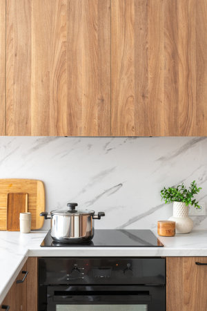 Wooden cabinets in modern kitchen. Vertical shot of stainless steel pot on a black induction stove...