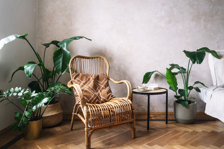 Rattan chair with brown cushion in corner of living room in bohemian style. Wooden armchair next to potted plants and side table with coffee cup and books. Cozy home interior with boho chic designの写真素材