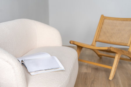 Selective focus at white sofa with open magazine on top, positioned near a wooden lounge chair in a modern living room. Modern and bohemian interior in apartmentの写真素材