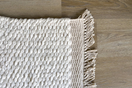 Flat lay of white woven rug with fringe detailing. Close up shot of carpet made from natural wool fiber material. Element of living room with textured, bumpy surface and a bohemian style floor decorの写真素材
