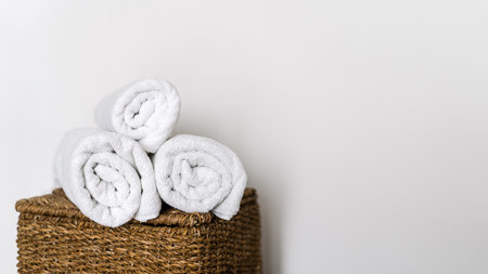 Fresh and soft rolled terry towels folded on top of wicker laundry basket. Bath accessories. Clean textile against white copy space wall in home bathroom. Concept of hygieneの写真素材