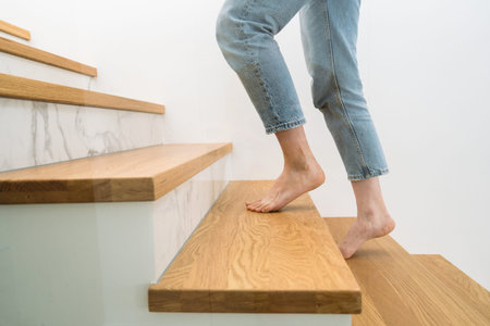 Barefoot woman standing on a wooden staircase at home. Cropped shot of female walking upstairs in...