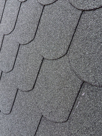 Vertical view of new asphalt shingles on a roof displays an organized pattern and textured surface. Bitumen tiles on rooftop, close up shot. Concept of renovation, repair and house improvementの写真素材