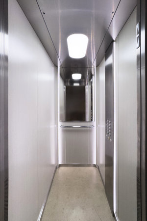 Empty passenger lift in a multi-story building, vertical shot . Modern elevator interior showcases metal walls, mirror and bright lighting inside cabinの写真素材