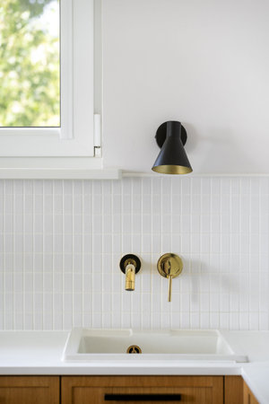 Vertical shot of a stylish kitchen showcases a gold faucet above a sink against textured white tiles...