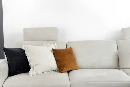 A minimalist living room features a comfortable, light-colored sofa adorned with decorative pillows in various colors and textures, creating a warm and inviting atmosphere in the bright setting.の写真素材