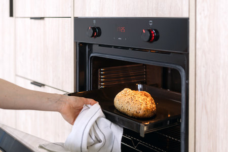 Persons hand removes a freshly baked loaf of bread from an oven, using a white towel. Home bakery concept. Female making homemade pastry food, cropped shotの写真素材
