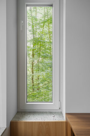 White and plastic window frame in serene interior with vibrant greenery from the forest on backgrounds. A view of nature from a country house, vertical shot. Elements of interior in apartmentの写真素材