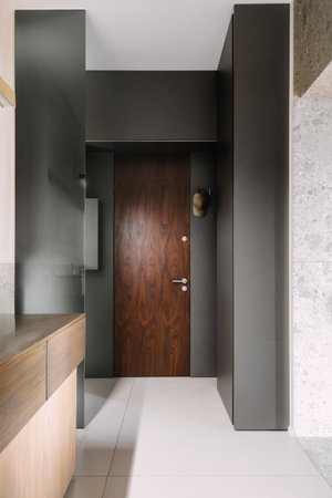 Vertical shot of apartment entry way features a polished wooden door against minimalist walls. Open space home with empty corridor and elegant interior designの写真素材