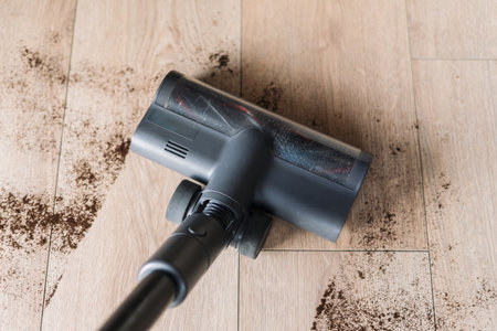 A person vacuuming up dirt and debris on hardwood floor, using a cordless vacuum cleaner at home. Flat lay shoot. Concepts of housework and household appliancesの写真素材