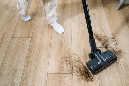 In a well-lit room, woman is actively vacuuming dirt off a wooden floor, demonstrating a commitment to maintaining cleanliness and orderの写真素材
