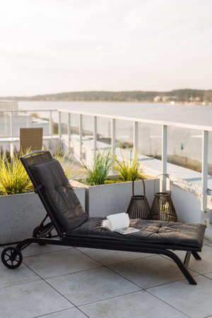 Open book on black lounger, vertical shot. Lounge chair with gray cushions on a rooftop patio...